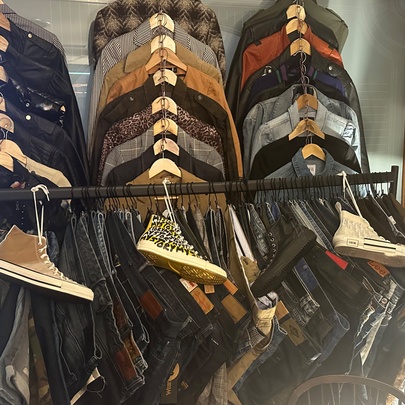 A rack of assorted casual apparel, including folded flannel or patterned shirts on hangers, jackets, and denim trousers with high-top sneakers displayed on top.