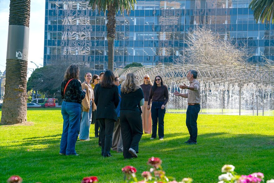 A group of people on a walking tour in front of a group leader in a park. 