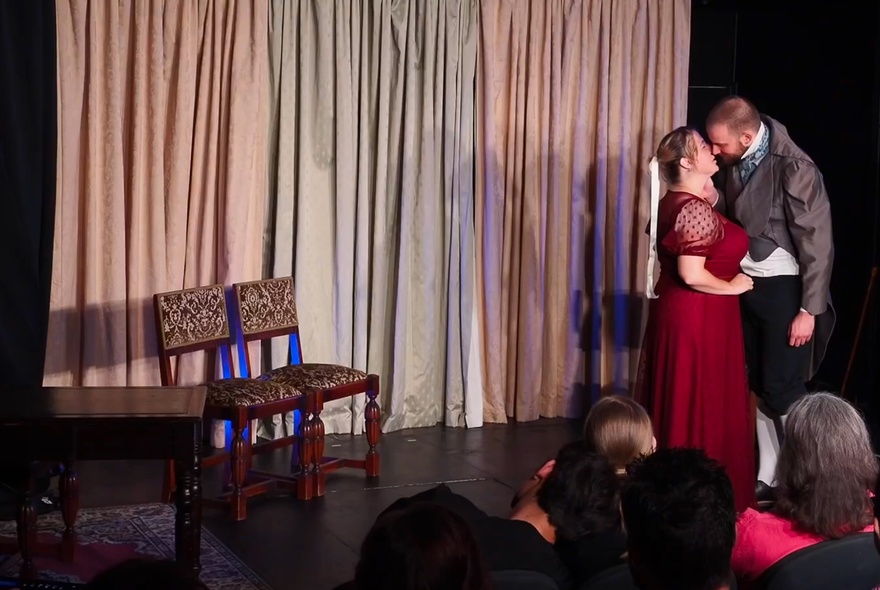 Two impro actors on stage in Regency clothing, acting out a scene in front of an audience.