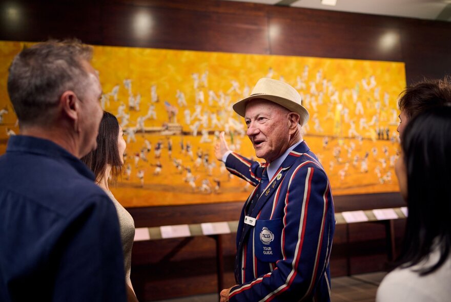 A tour guide in a striped blazer pointing at a mural artwork for a tour group.