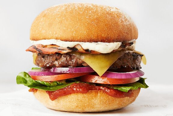 Close up of a burger, with cheese, egg, lettuce and tomato between two buns.