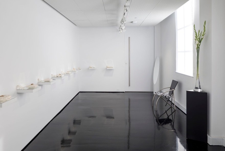 Jewellery displayed on white shelves in a white gallery space with shiny black floor.