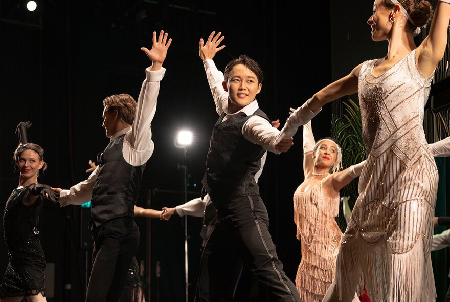 Dancers wearing 1920s waistcoats and fringed gowns, performing on stage.