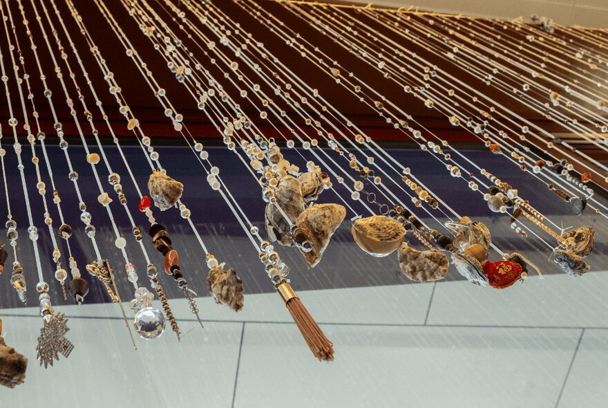 Artwork detail of items threaded on rope, suspended from above.