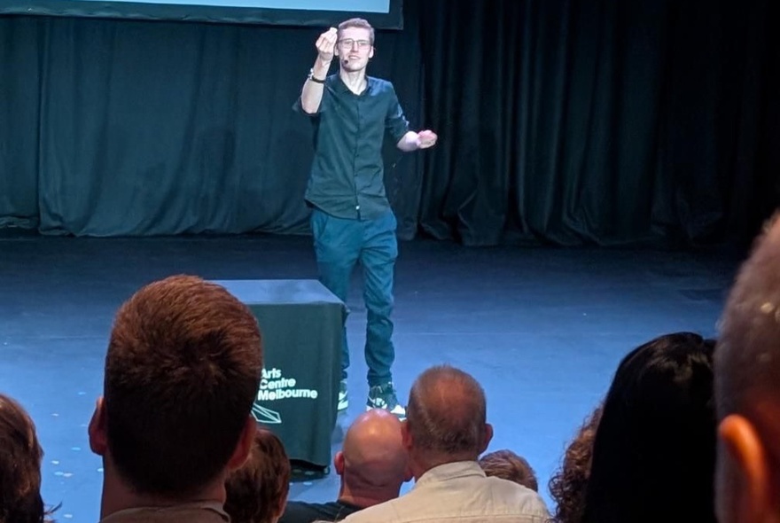 A magician standing on a stage performing in front of an audience.