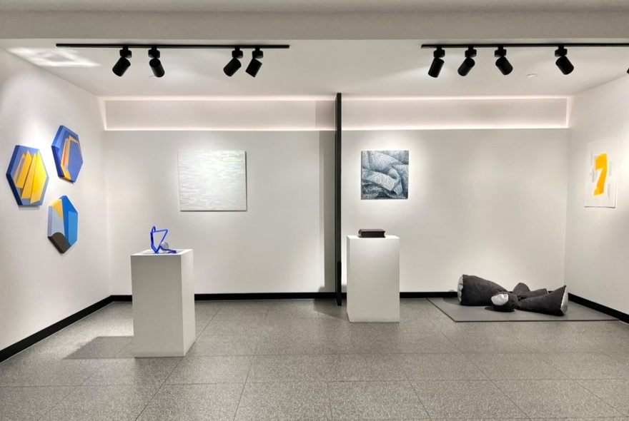 A gallery space featuring colouful artworks on the white walls and white pedestals.
