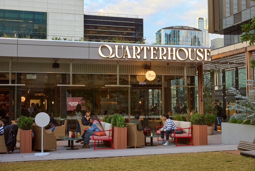 People sitting at an indoor-outdoor bar with a grass lawn and a sign that says Quarterhouse.