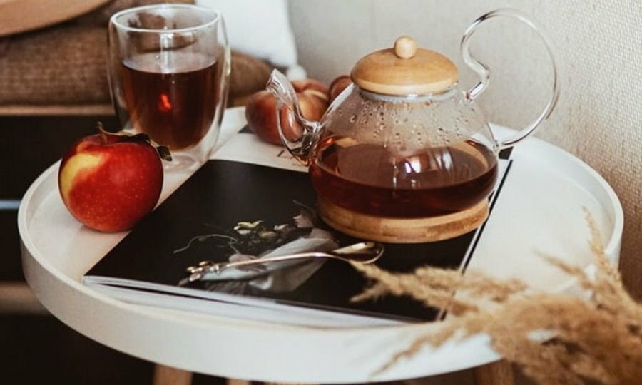 A tea pot on a small table with mugs and magazines beside it