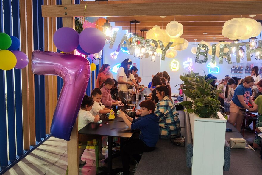 A room set up for a kid's birthday party with the party goers seated at tables and playing with slime.