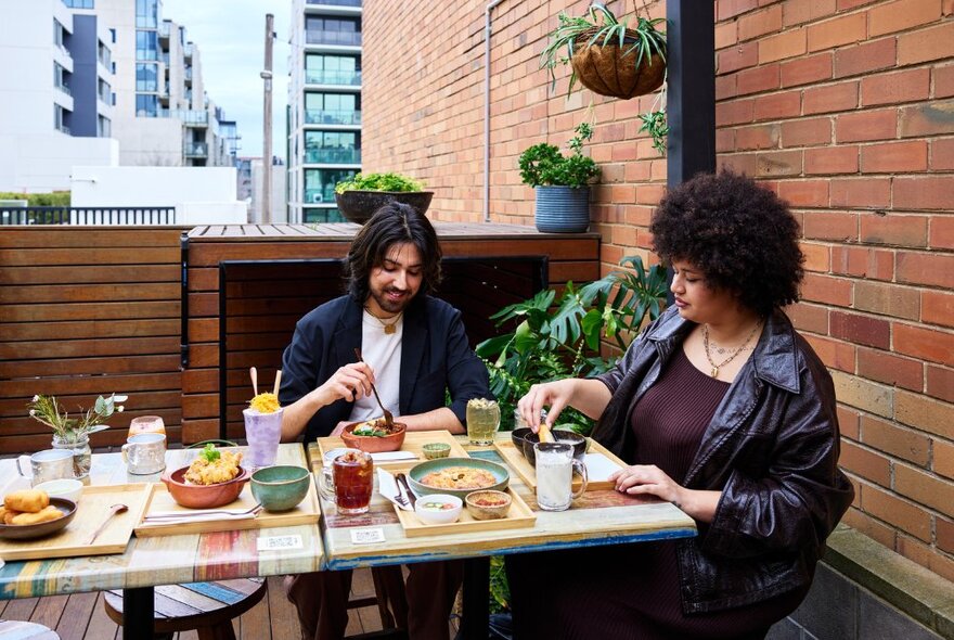 Two people enjoying multiple Thai dishes outside.