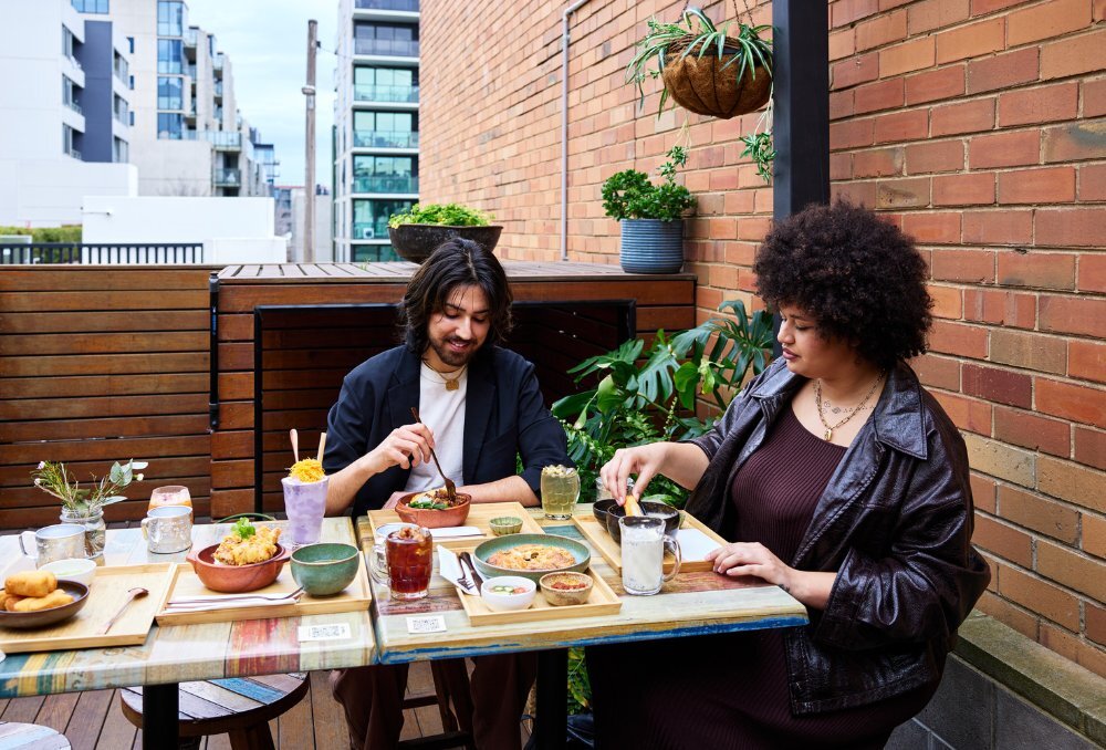 Two people enjoying multiple Thai dishes outside.