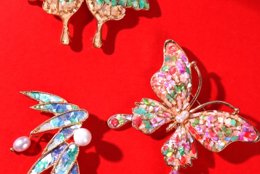 Three decorative brooches that use mother of pearl inlay, on a red background.