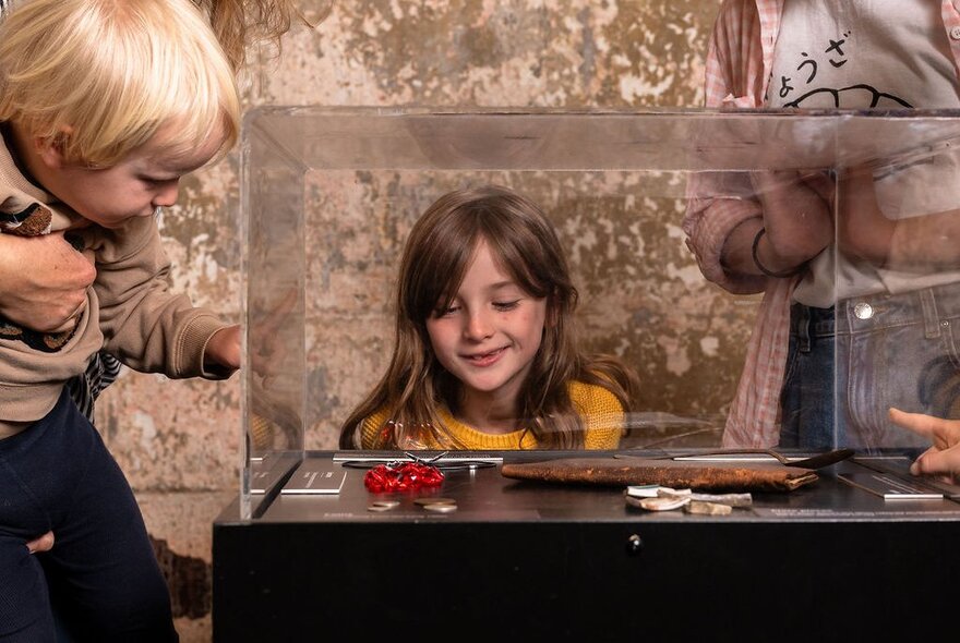 A young girl and a very small boy looking at a glass case displaying old-fashioned weapons at the Old Melbourne Gaol.