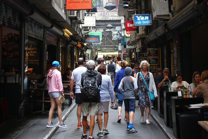 Melbourne city laneway with diners seated at outdoor tables and people walking past the diners along the centre of the lane.