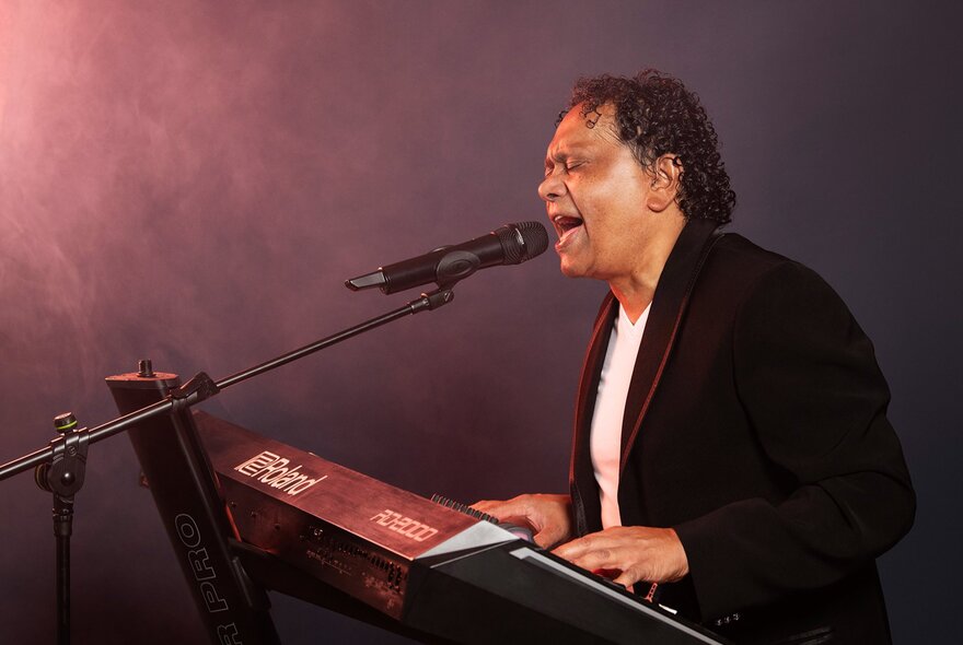 Soul musician Dinash Daniel playing a piano keyboard and singing into a microphone in a studio setting.