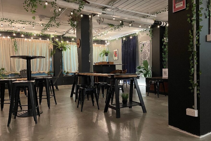 Industrial venue with barstool seating, curtained area and overhead fairy lighting.