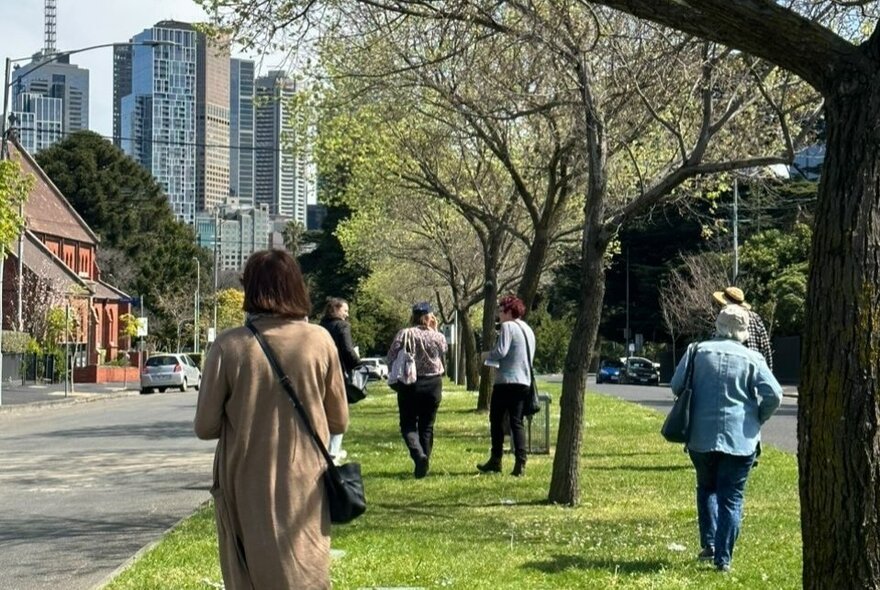 People walking along a leafy median strip in East Melbourne with city buildings in the background.
