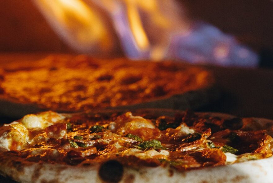 Two pizzas cooking in a wood-fired oven.