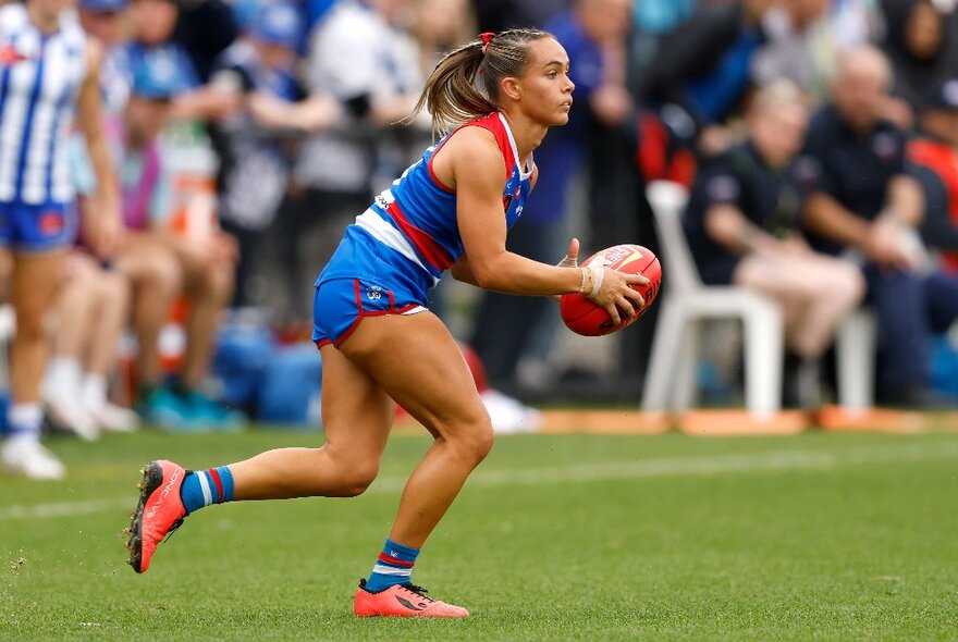 Female AFL football player about to kick a red ball during a match.