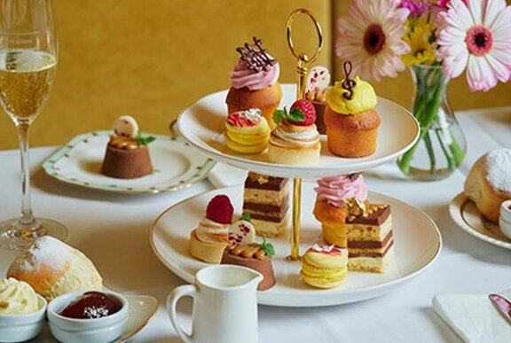 A table set for high tea with a tiered cake plate, a glass of champagne, flowers and other treats.