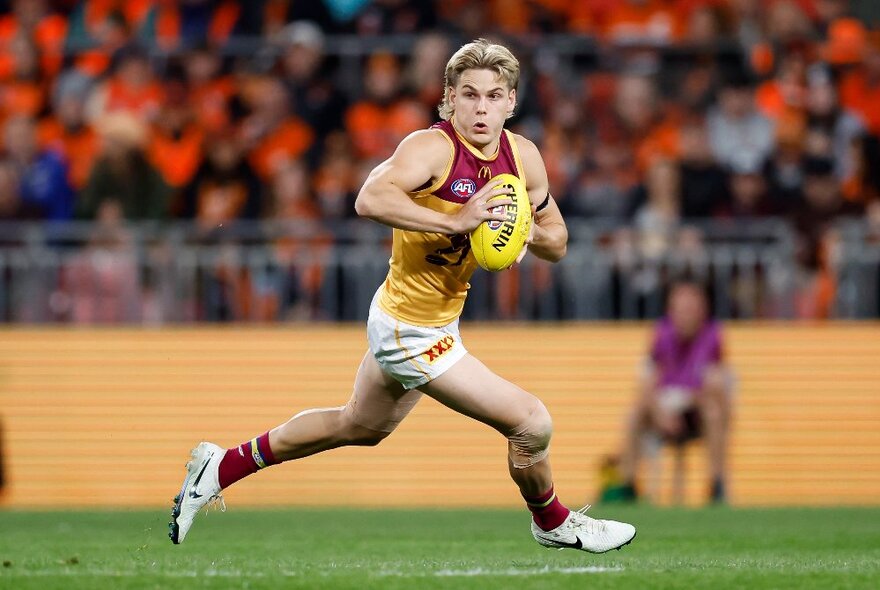 A Brisbane Lions player running with a yellow football. 