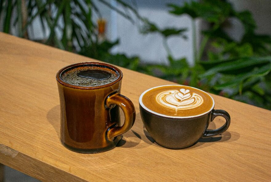 A brown mug and a cappuccino with late art on a wooden slim tabletop. 