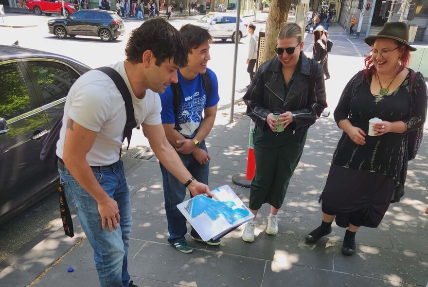 Tour leader showing three walking tour participants a page from an open notebook he holds, on a Melbourne city footpath.