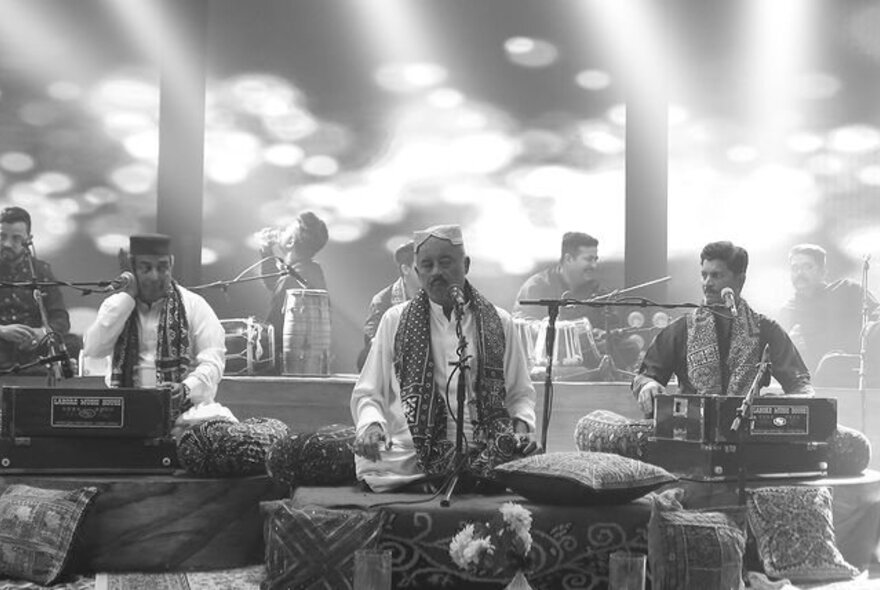 A black and white image of Sufi musicians sitting and performing on their instruments. 
