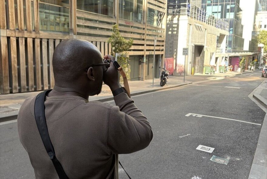Man taking a photograph in a Melbourne street with unusual wood-fronted building.