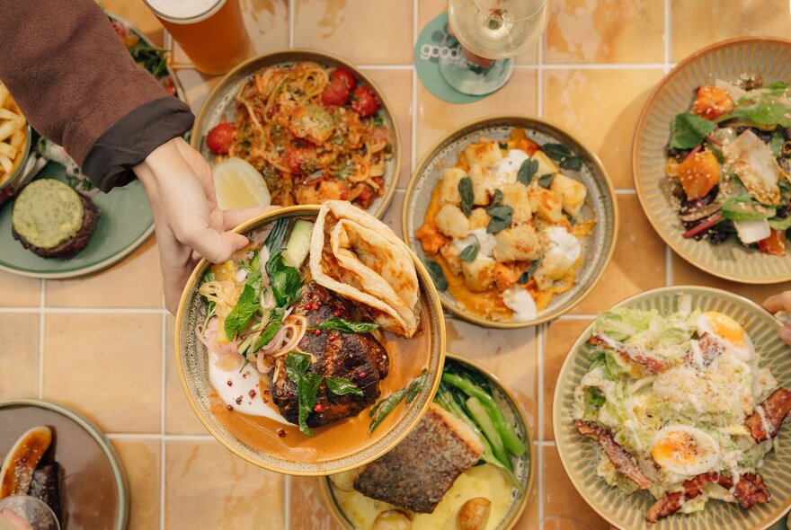 A hand passing a plate of food over a table filled with pates of food.