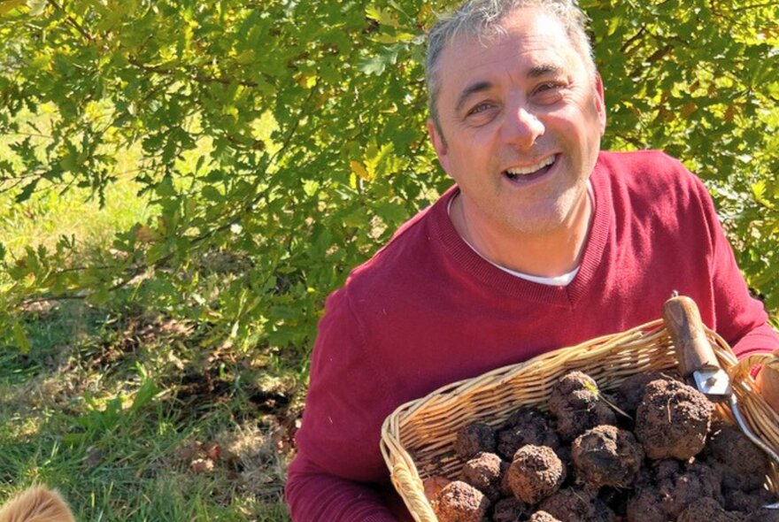 Chef Christophe Grégoire outdoors smiling, holding a basket of freshly harvested truffles.