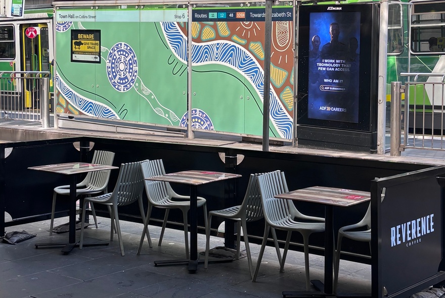Small outdoor seating area on a Melbourne city street, a tram stop in the background.