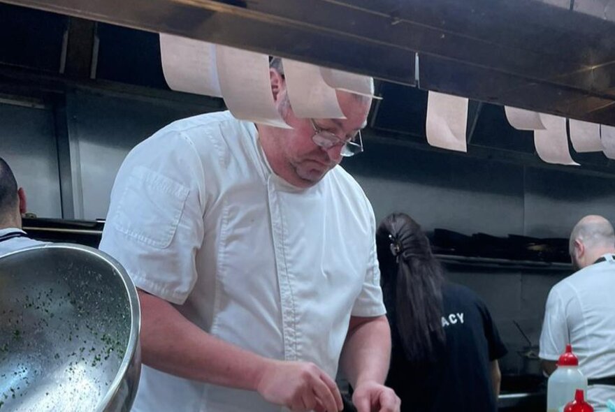 A chef wearing a white chef's uniform preparing food in a commercial kitchen.