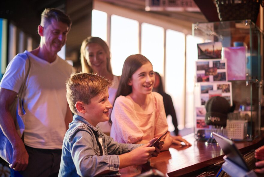 Two kids smiling at a counter with parents looking on in the background. 