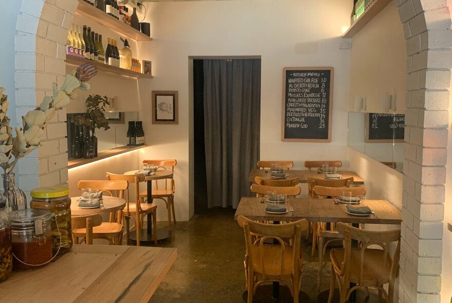 Restaurant interior with brick arched wall and several wooden tables.