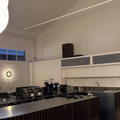 Modern and minimalist cafe interior featuring a dark countertop, white walls, and speaker systems mounted high on the wall.