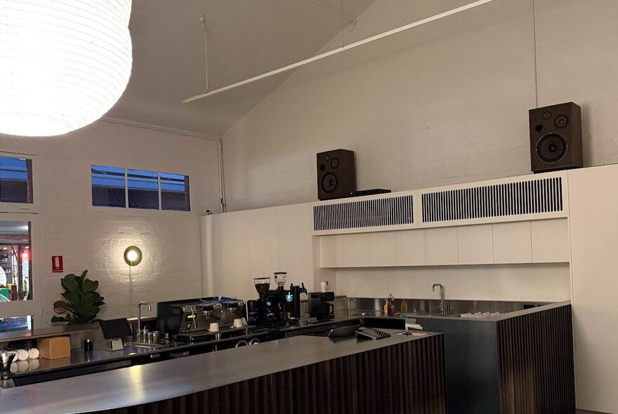 Modern and minimalist cafe interior featuring a dark countertop, white walls, and speaker systems mounted high on the wall.