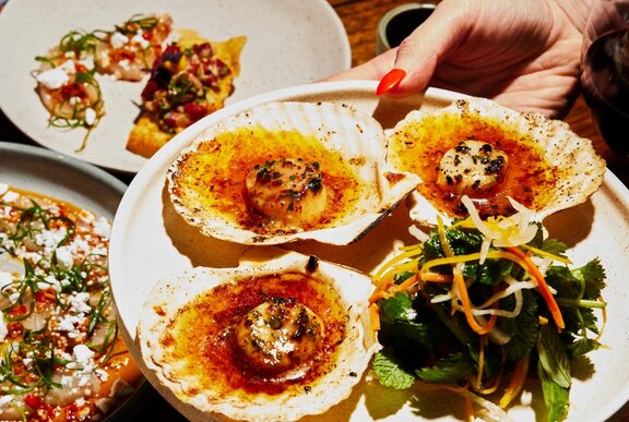 A plate of scallops being placed on a restaurant table set with dishes. 