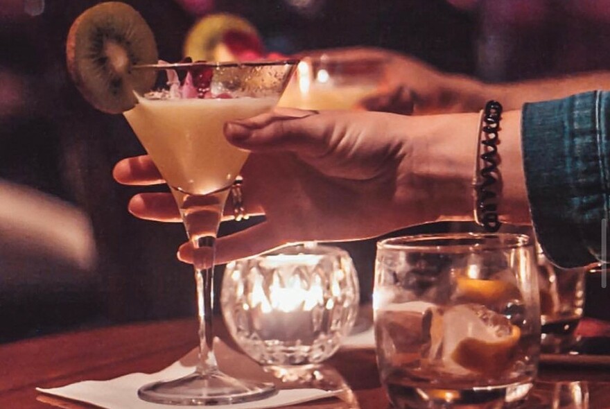 Person holding a cocktail with kiwifruit garnish.