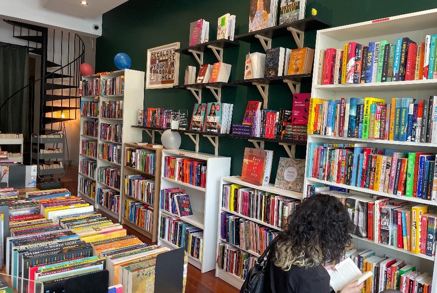 Small bookshop crammed with shelves and rows of books, person browsing in foreground.