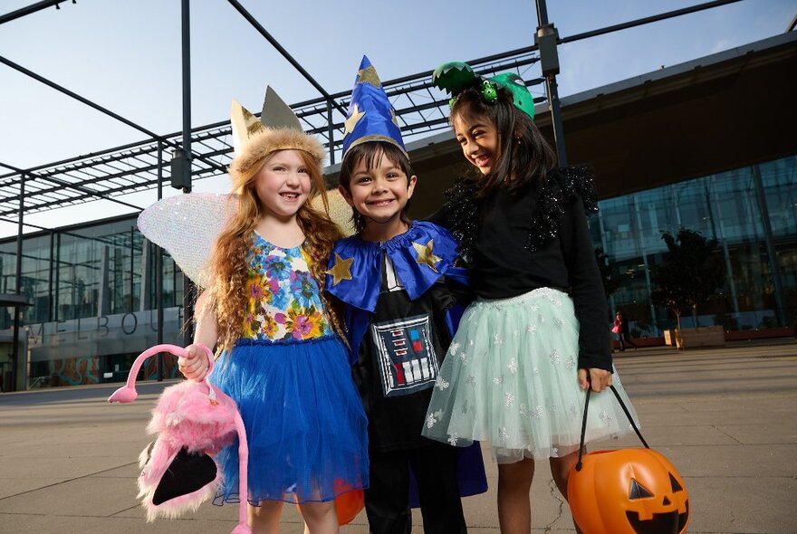 Three children dressed in Halloween costumes standing outside the entrance to Melbourne Museum.