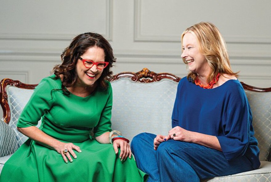 Annabel Crabb and Leigh Sales sitting on a couch, both of them laughing.