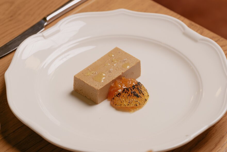 A slice of terrine served on a white plate with a fruit or citrus gel accompaniment.