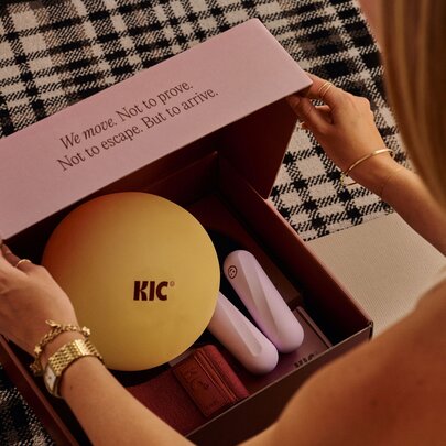 A person opening a Pilates starter kit featuring a round Pilates ball and other essential equipment in a pink box.