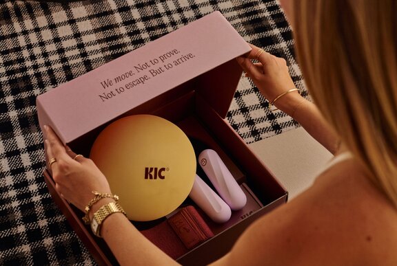 A person opening a Pilates starter kit featuring a round Pilates ball and other essential equipment in a pink box.