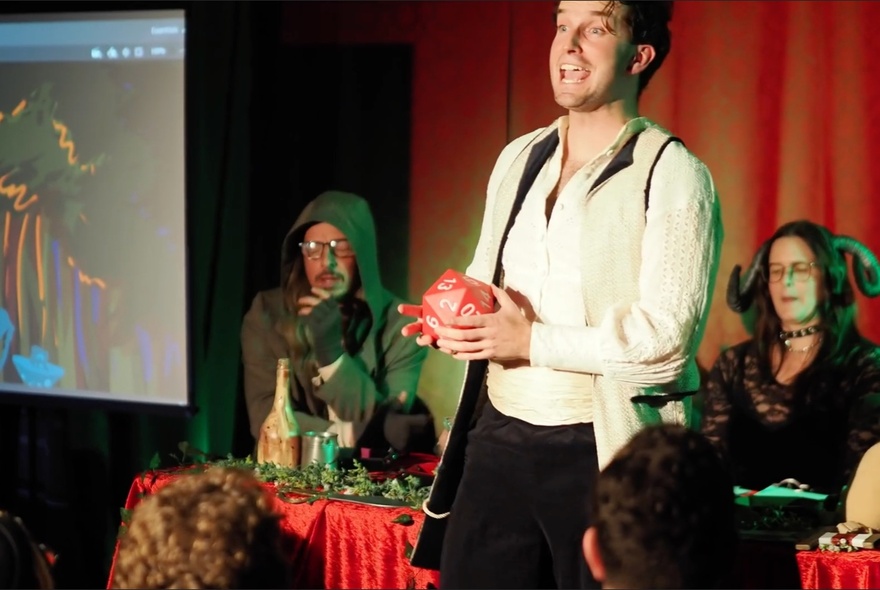Performer standing holding a cube in front of a row of seated fellow performers.
