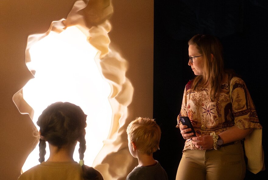 Tour guide and children peering into a cavelike opening in a museum exhibit.