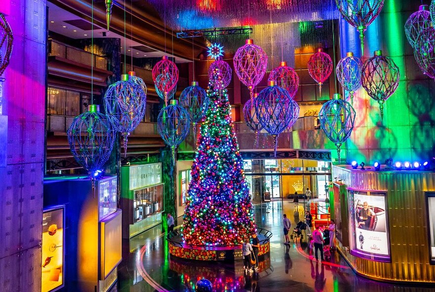 A giant Christmas tree with multicoloured lights in a large foyer with colourful lantern decorations hanging from the ceiling.