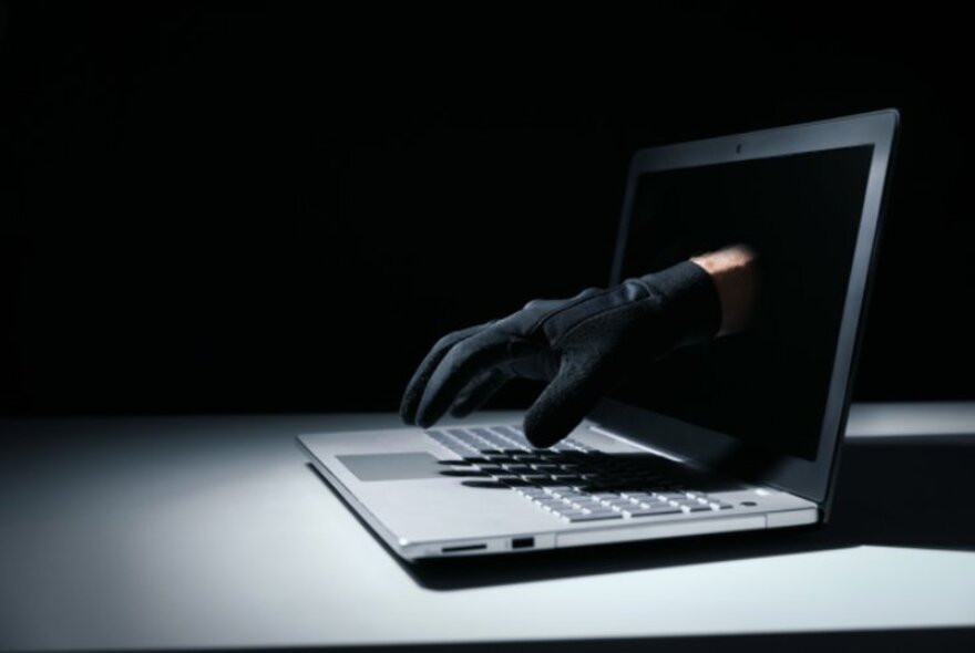 A black-gloved hand reaching out from a laptop computer screen.