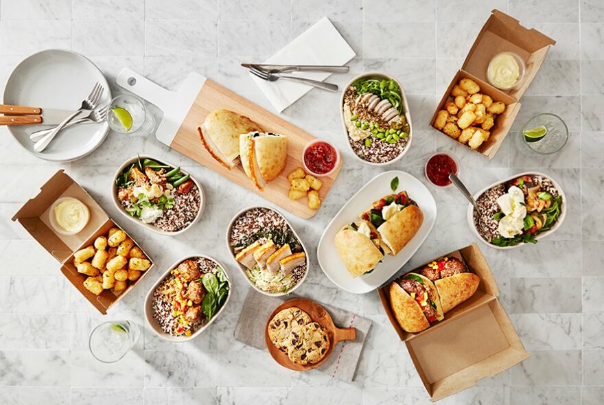 A table covered in takeaway containers with sandwiches, wholebowls and potato gems